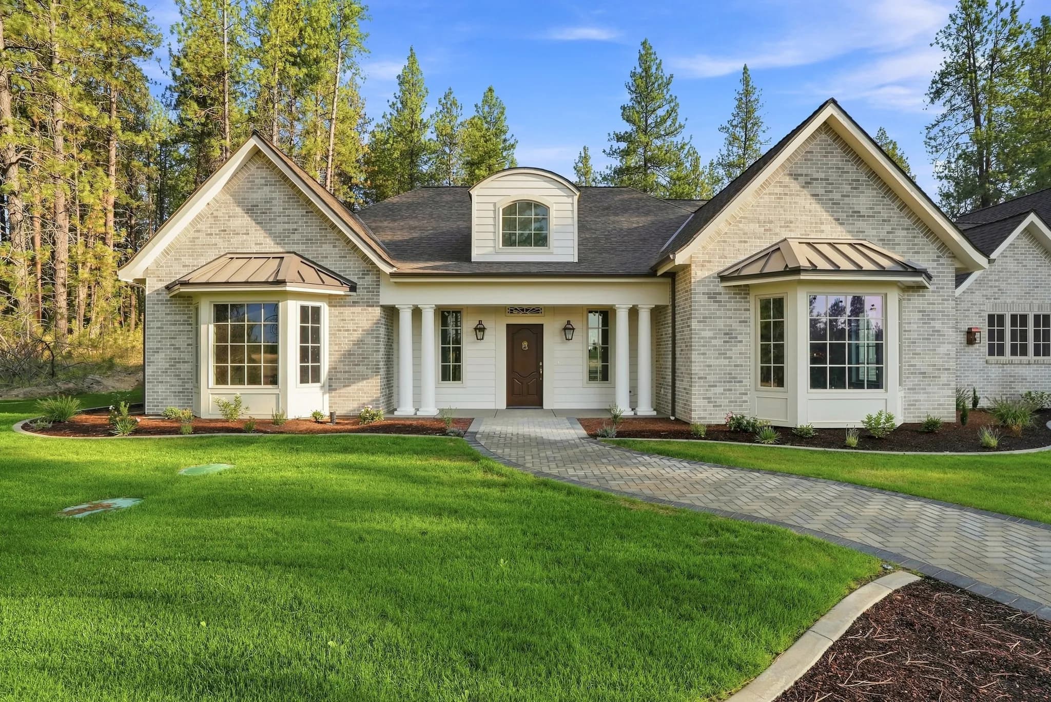 Brick custom home by JM Homes with copper-roofed bay windows and a columned front porch