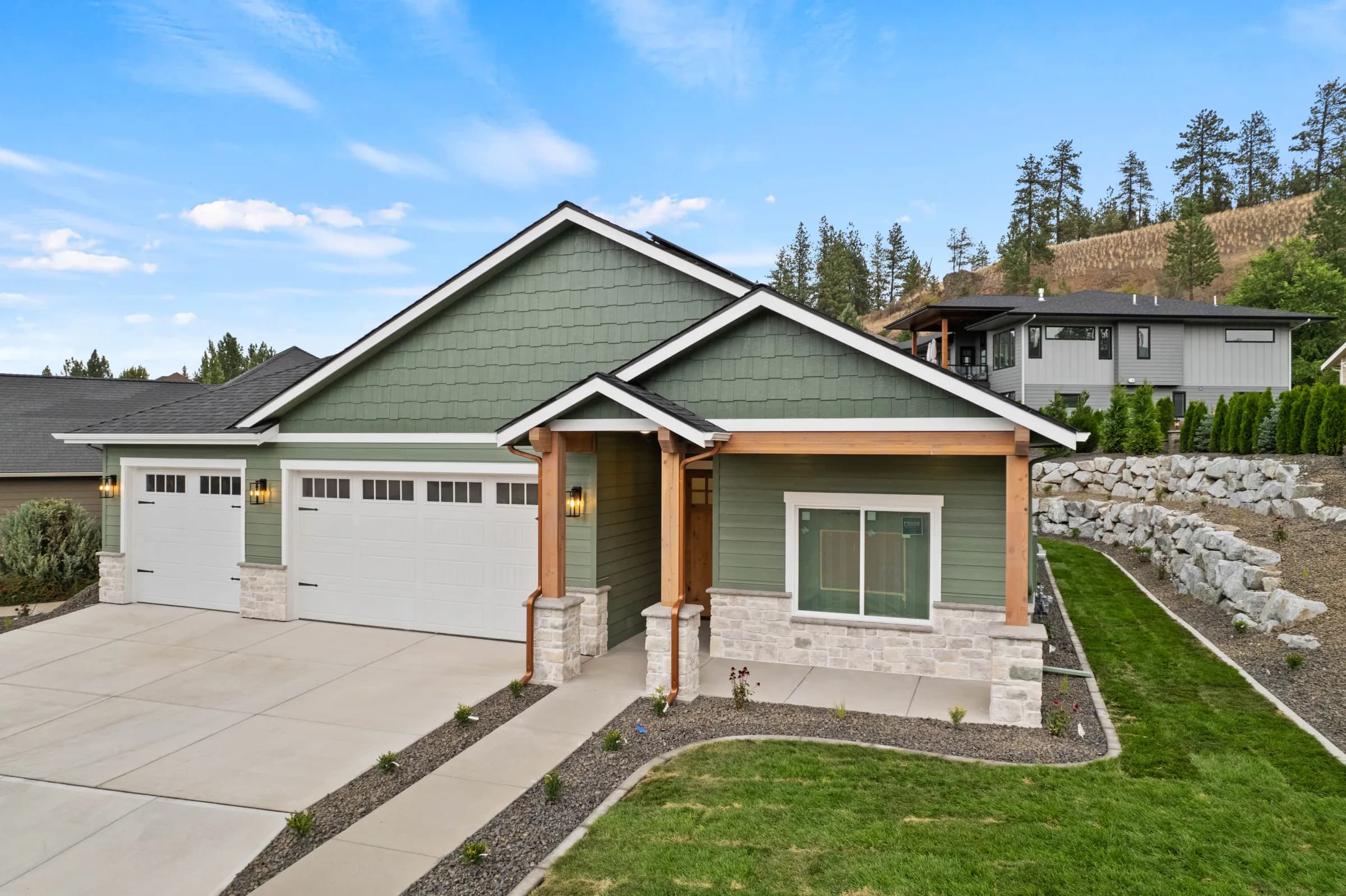 Craftsman on a sloped lot with terraced boulder retaining walls and pines above